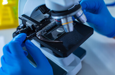 Closeup shot of microbiology defective sample on glass plate placing under microscope zooming lens while scientist hands wearing protective safety rubber gloves adjusting camera focus in laboratory
