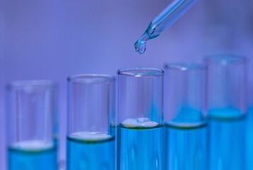 Closeup studio shot of scientific lab glass dropper dropping blue reagent solvent solution liquid sample into glassware test tube line in rack for analyzing science experiment in hospital laboratory