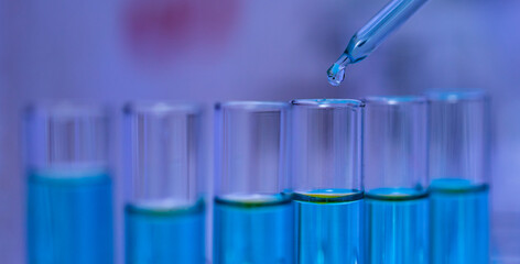 Closeup studio shot of scientific lab glass dropper dropping blue reagent solvent solution liquid sample into glassware test tube line in rack for analyzing science experiment in hospital laboratory