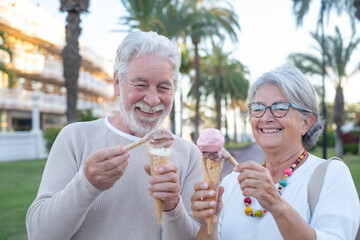 Happy adult mature retired couple having fun eating icecream cone in the park. Joyful elderly lifestyle concept. Two senior people white haired laughing enjoying free time