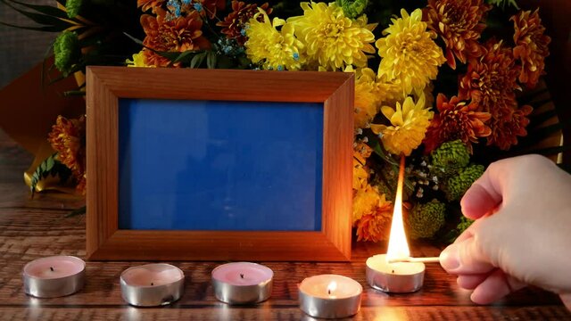 bouquet of chrysanthemum with wooden frame for photo on wooden background with burning candles, concept of memory, funerals and condolence