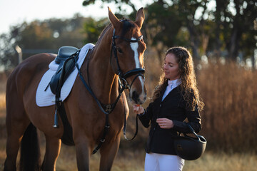 Young woman with curly hair feeding her horse in a sunny morning