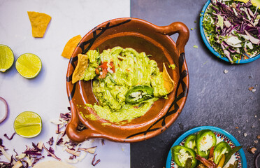 Delicious spicy guacamole in traditional clay pot above black and white surface