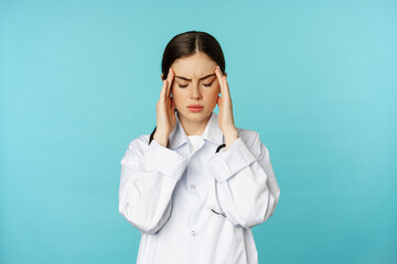 Image of woman doctor, medical personel grimacing from discomfort, having headache, migraine, feeling deezy, standing over torquoise background