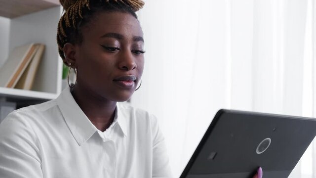 Online education. African woman. Digital technology. Concentrated lady scrolling tablet computer in light room interior.