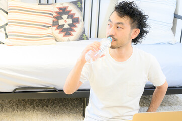A man sipping water while working in his room.