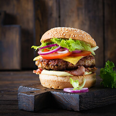 Hamburger with bacon, turkey burger meat, cheese, tomato and lettuce on wooden background. Tasty...