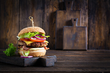Hamburger with bacon, turkey burger meat, cheese, tomato and lettuce on wooden background. Tasty...