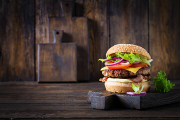 Hamburger with bacon, turkey burger meat, cheese, tomato and lettuce on wooden background. Tasty...