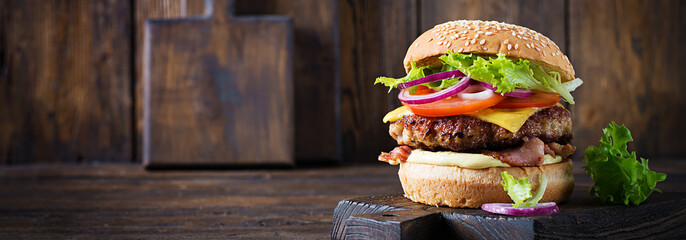 Hamburger with bacon, turkey burger meat, cheese, tomato and lettuce on wooden background. Tasty burger. Close up - obrazy, fototapety, plakaty