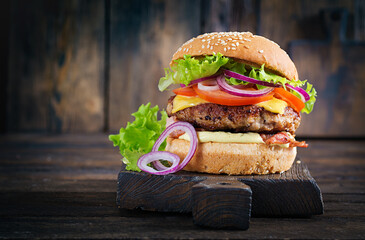 Hamburger with bacon, turkey burger meat, cheese, tomato and lettuce on wooden background. Tasty burger. Close up