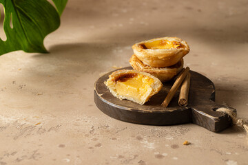 Pasteis de Belem,  portuguese egg tart pastries  on wooden cut board on beihe backround with monstera  leaf.