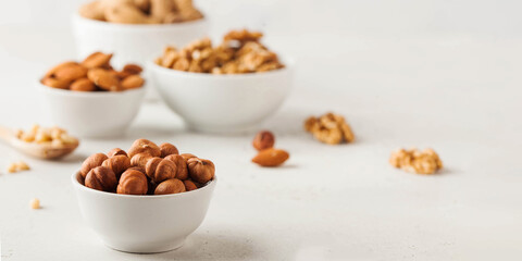 Hazelnuts and other nuts in white bowls on a white background. Banner