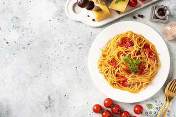 Spaghetti with tomatoes, parmesan and basil in a white plate on a bright kitchen table. Traditional Italian pasta with vegetables and cheese