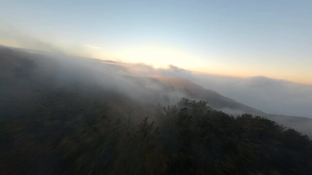 FPV aerial footage of a beautiful sunset with fog in a coastline mountains