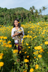 A young girl enjoys the lush beauty of the beautiful yellow marigold flowers of a medical field, with a flower behind her ear.