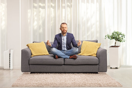 Young Man In Suit And Jeans Meditating On A Sofa At Home