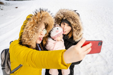 Two caucasian women and baby girl taking selfies mother with her small child and her friend or aunt...