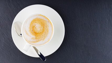 Cup of coffee on a dark background. Coffee on a slate board. Cup of morning coffee on a white saucer. Top view. Copy space