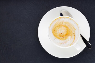 Cup of coffee on a dark background. Coffee on a slate board. Cup of morning coffee on a white saucer. Top view. Copy space