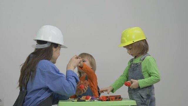 Woman and two children with protection helmet work at tools table, happy learn, different gender occupation, equal opportunity
