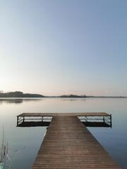 Wooden platform on the lake. Horizon, blue water and clear sky at the dusk. Blue background and space for text. 