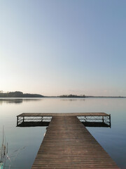 Naklejka premium Wooden platform on the lake. Horizon, blue water and clear sky at the dusk. Blue background and space for text. 