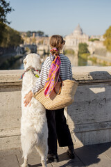 Woman enjoying beautiful view of Rome city and Vatican standing together with dog on the bridge....
