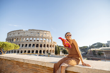Portrait of a cheerful woman on background of Coliseum in Rome on a summer time. Concept of visiting famous landmarks and travel Italy. Girl wearing dress and colorful shawl