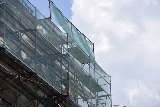 Building facade under renovation works with construction scaffolding frame covered with protective net for workers safety