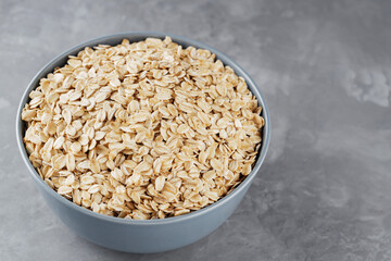 Bowl of oat flakes on gray background. Dry rolled oats in a gray bowl. Raw oatmeal flakes. Copy space. Top view