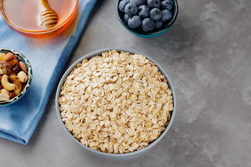 Healthy breakfast oatmeal with berries, nuts and honey. Oat flakes, blueberries, honey and assorted nuts on a gray background. Vegan breakfast with oatmeal. Top view