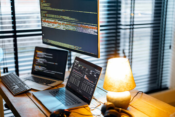 Cozy workplace with lapto and desktop computers with programming code on the screens. Programmer...
