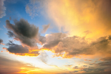Dramatic yellow sunset landscape with puffy clouds lit by orange setting sun and blue sky.