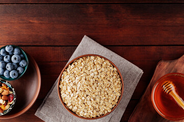 Dry oatmeal flakes, blueberries, honey and assorted nuts on a wooden background. Cereal and various delicious ingredients for breakfast on a boards. Copy space. Top view