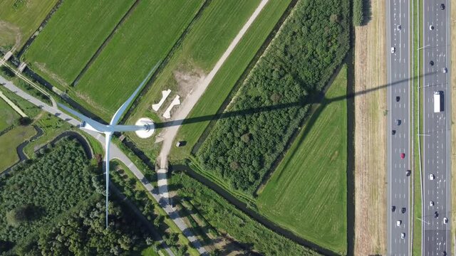 Aerial top down view of wind turbine and highway windtower creating sustainable energy by converting kinetic power from natural resources road two way traffic vehicles moving both ways 4k quality