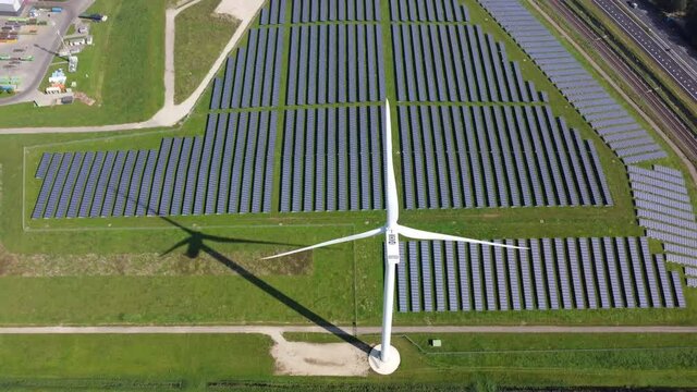 Aerial high altitude view of wind-turbine and solar panels in the background both providing green clean renewable energy by resources from natures wind and sun for sustainability 4k resolution quality