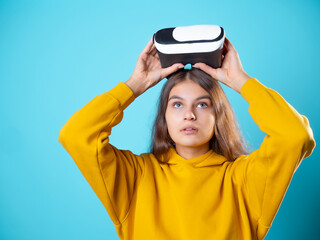 Fototapeta na wymiar VR gamer, a young woman in a youth outfit uses a virtual reality helmet. A brunette in yellow on a blue background puts a vr gadget on her head