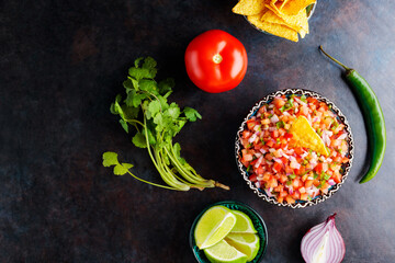 Pico de Gallo salsa and ingredients. Bowl of tasty Pico de Gallo salsa on dark background. Mexican cuisine concept. Top view. Copy space
