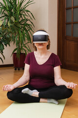 Senior woman sitting on yoga mat meditating in VR glasses at home. Active elderly, futuristic lifestyle, mental health.