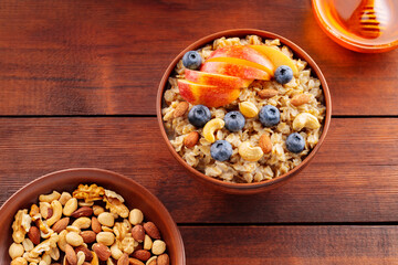 Oatmeal porridge with blueberries, apple slices and nuts on a wooden boards. Oatmeal, various nuts, and honey for a healthy breakfast. Top view. Copy space