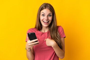 Naklejka premium Young woman using mobile phone isolated on yellow background with surprise facial expression