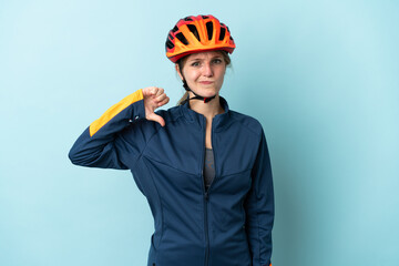 Young cyclist woman isolated on blue background showing thumb down with negative expression