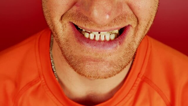Crop man with diastema and toothy smile. Closeup high angle of unrecognizable redhead male with gaps between teeth on red background in studio