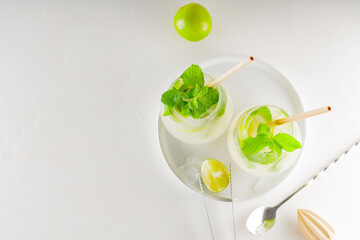 Mojito cocktail with lime and mint on a white background. Drink making tools and ingredients for cocktail. Two glasses of mojito on a white plate. Top view. Copy space