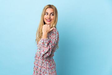 Young Uruguayan blonde woman over isolated blue background pointing to the side to present a product