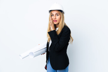 Young architect woman with helmet and holding blueprints over isolated white background whispering something
