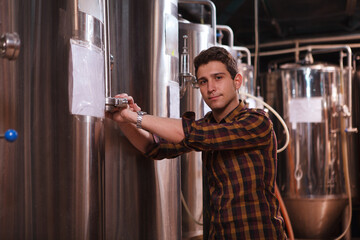 Professional brewer looking to the camera while working at his microbrewery, copy space