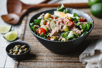 Canned tuna salad with fresh vegetables, capers and olives in a black bowl. Healthy lunch or dinner. - 480540015