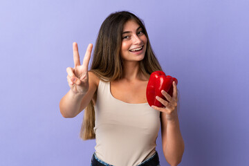 Young woman holding a pepper isolated on purple background smiling and showing victory sign